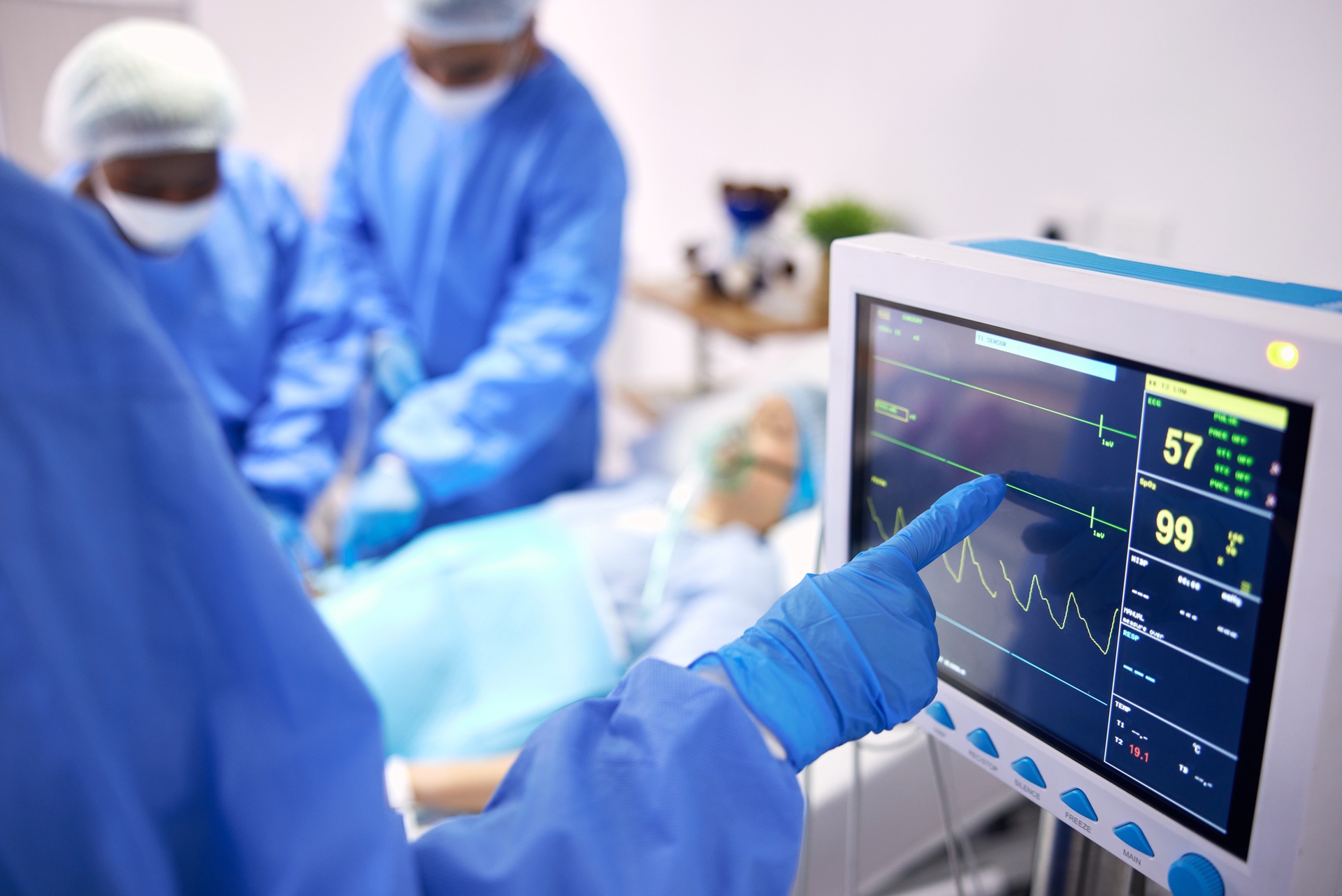 Medical staff in surgical attire monitor a patient’s vital data using a monitor.